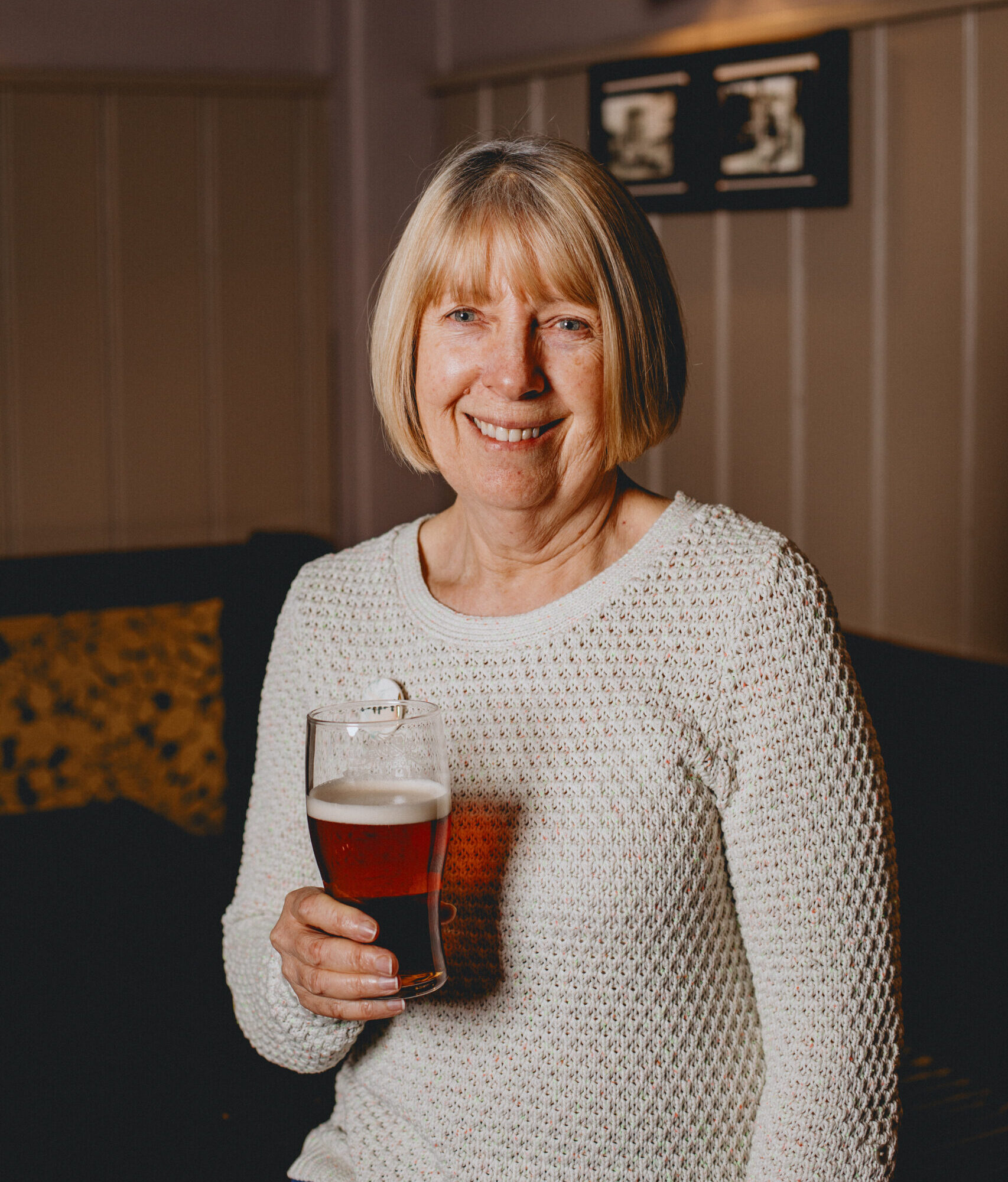 A woman stood up holding a pint of Bitter.