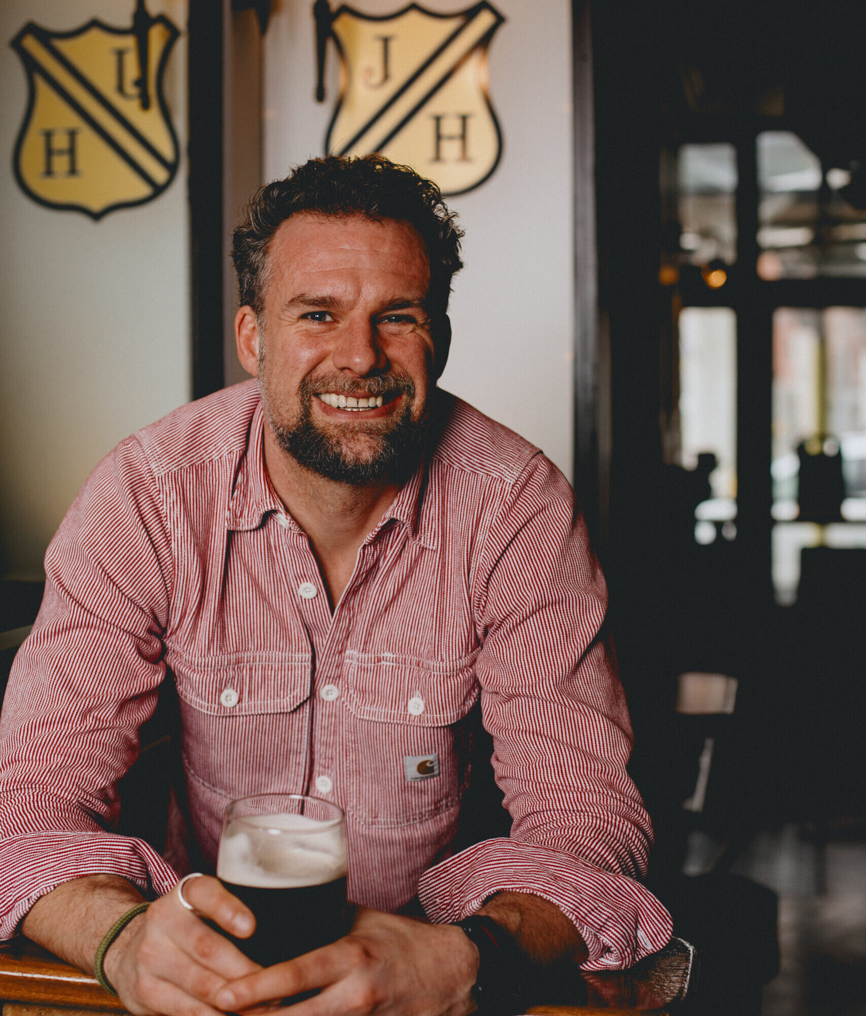 A man leaning over smiling holding a pint of Bitter.
