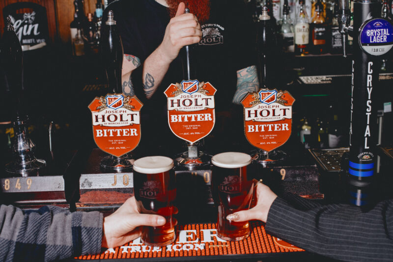 Two people holding pints of Bitter at the bar.