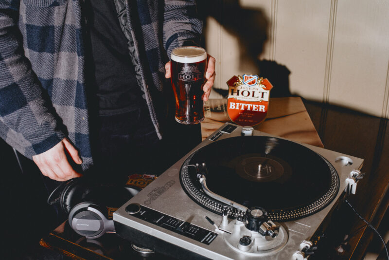 A man holding a pint of Bitter next to an LP player.