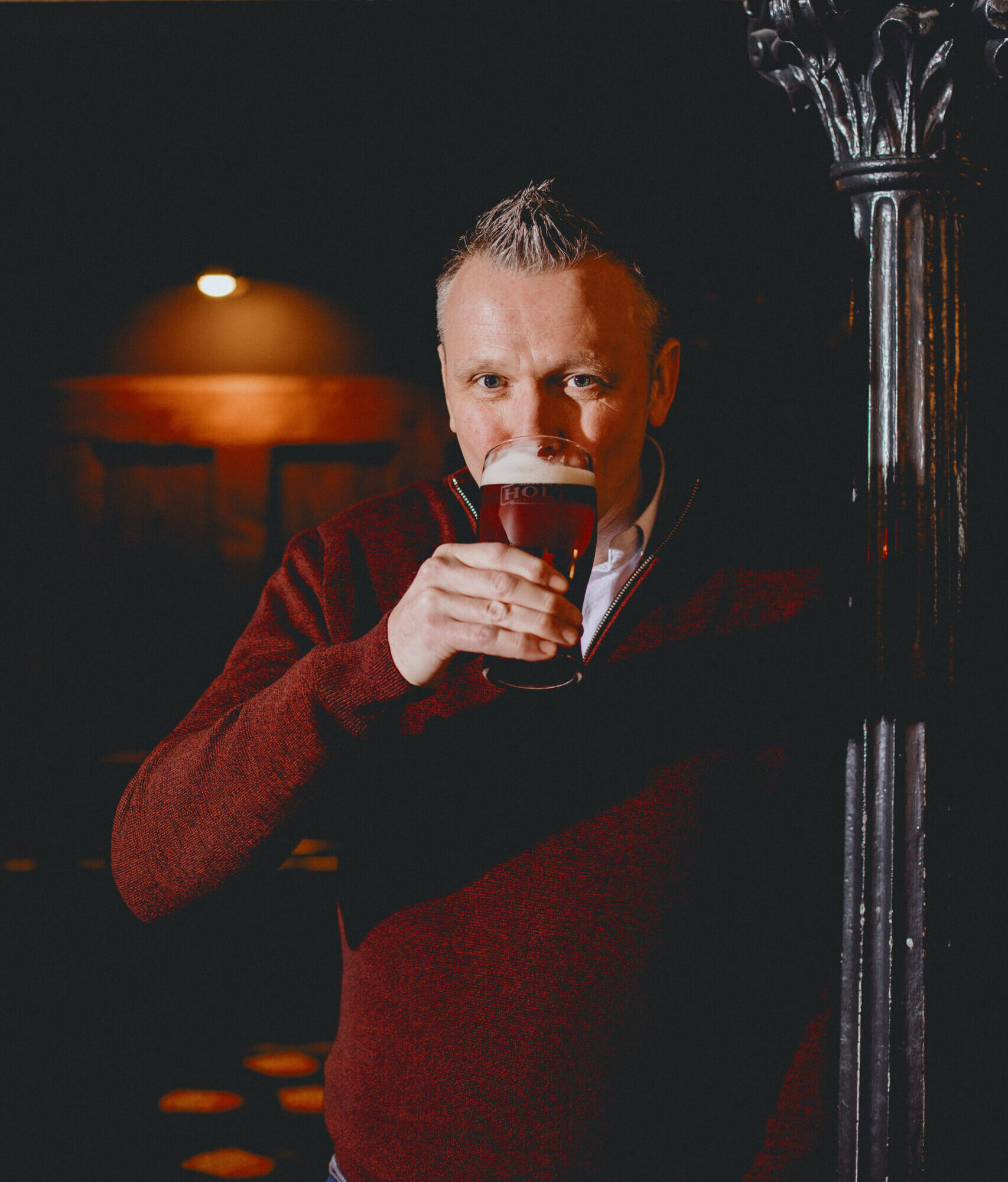 A man stood up dressed in red drinking Bitter.